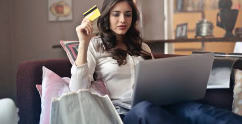 Woman shopping online. A woman is sitting on the couch looking at something a silver laptop and holding a bank card in her right hand.